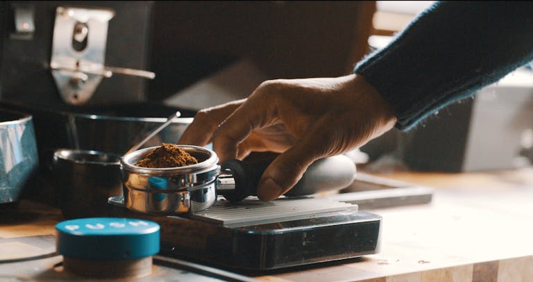 Close-up of a barista's hand preparing coffee grounds with precision in a modern kitchen.