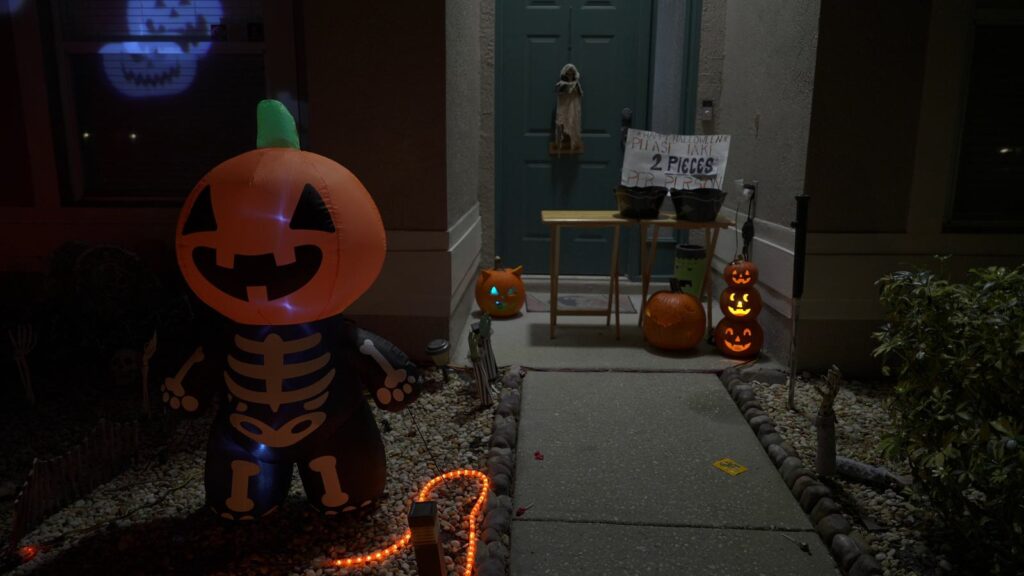 Front walkway of a home decorated for Halloween at night with jack-o-lanterns, orange rope lights and an inflatable pumpkin skeleton