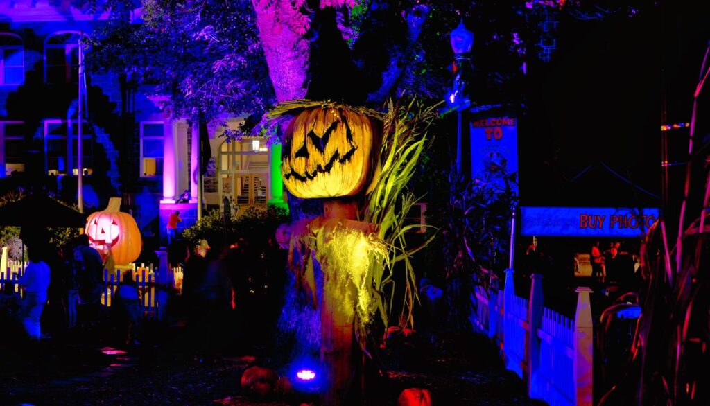 Glowing jack-o'-lantern scarecrow and purple-lit trees at a free Halloween festival near Portland