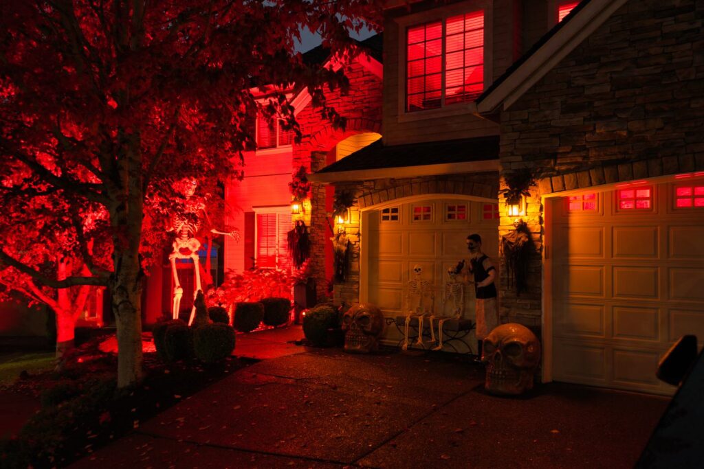 House lit red for Halloween with skeletons and giant skulls on the driveway in a Portland-area neighborhood