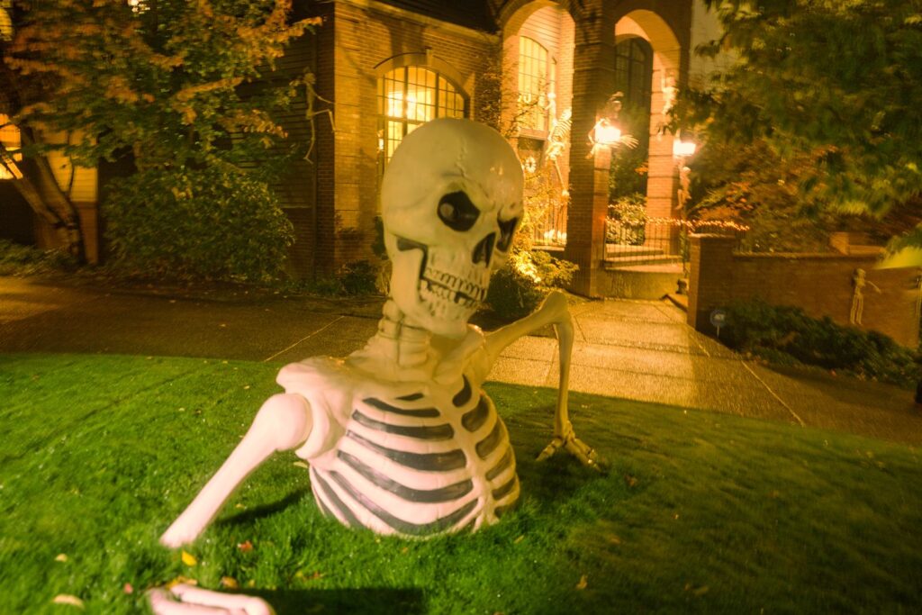 Giant skeleton climbing out of a front lawn outside a decorated brick home at night