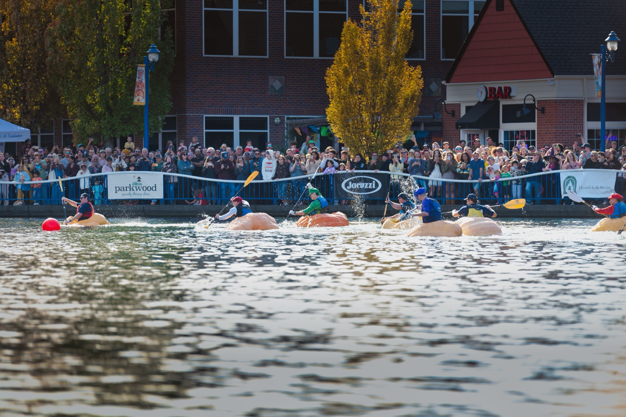 Racers in giant pumpkins paddling around the turn on the lake during the first race