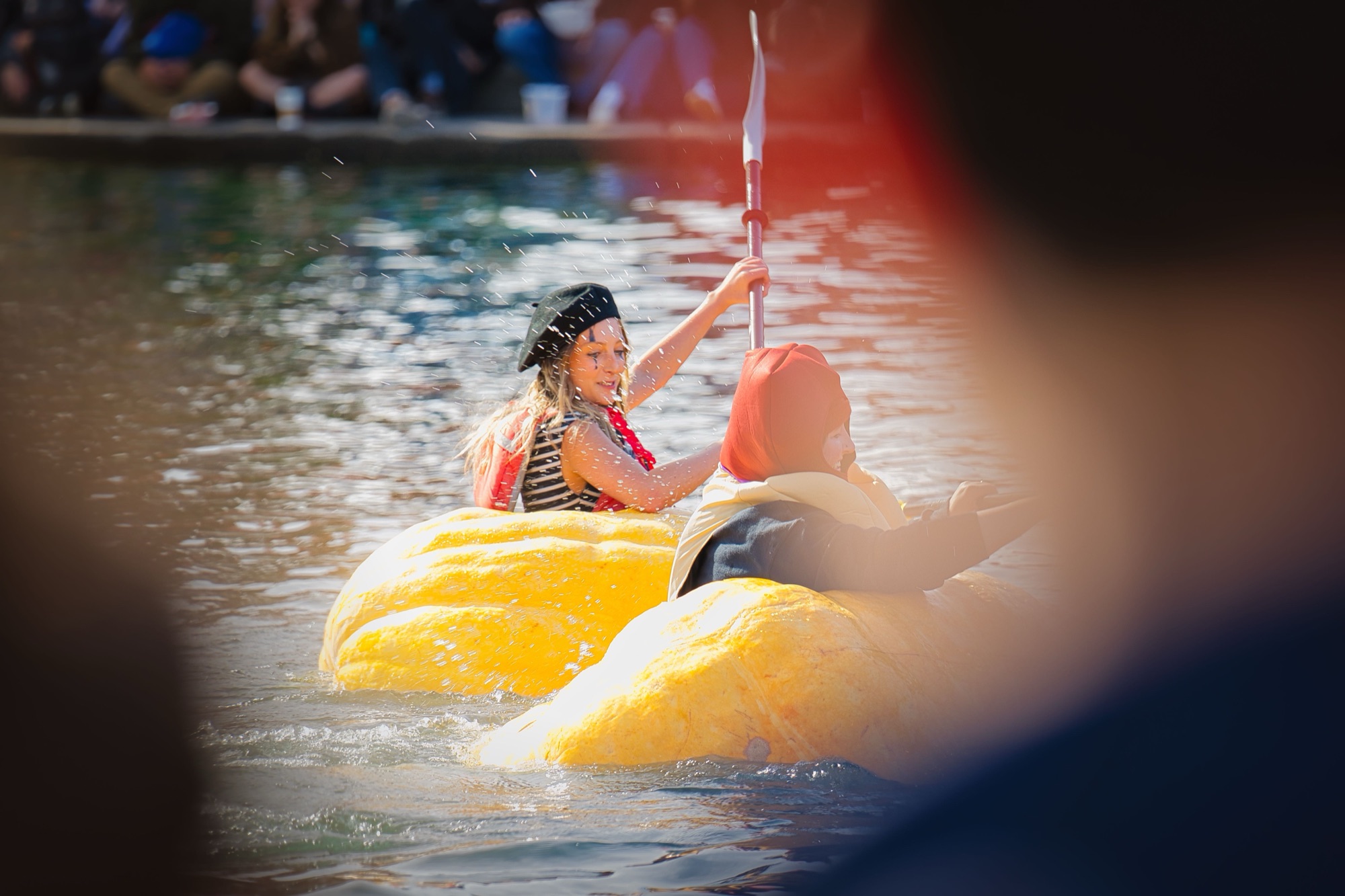 A mime and a hot dog paddling their giant pumpkins side by side